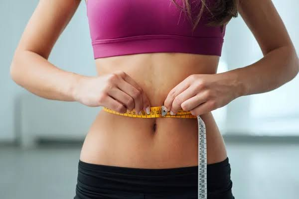 Woman measuring her waistline with a tape measure as part of a weight-management routine